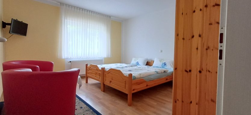 Schlafzimmer 2 Helles Zimmer mit zwei Betten, einem Fernseher und roten Sessel.