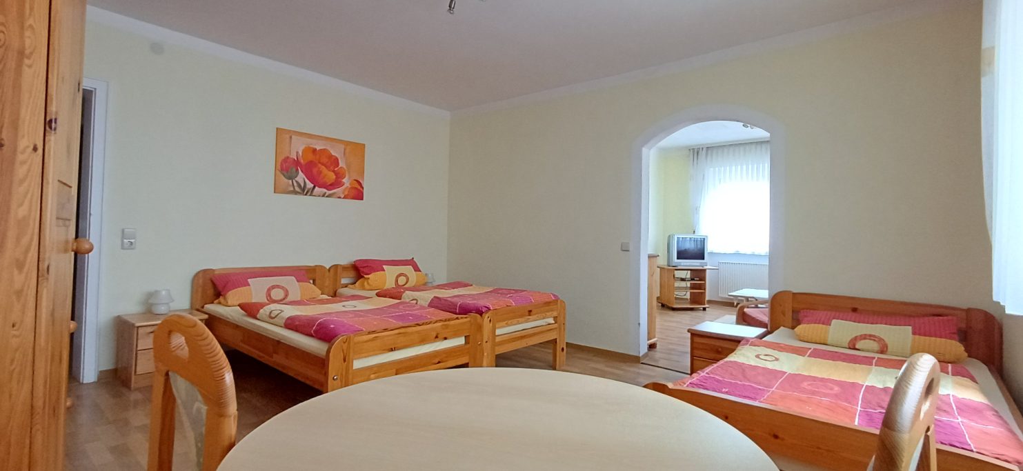 3 Bettzimmer Helles Zimmer mit drei Betten, Tisch und Stühlen, freundliche Farbgestaltung.