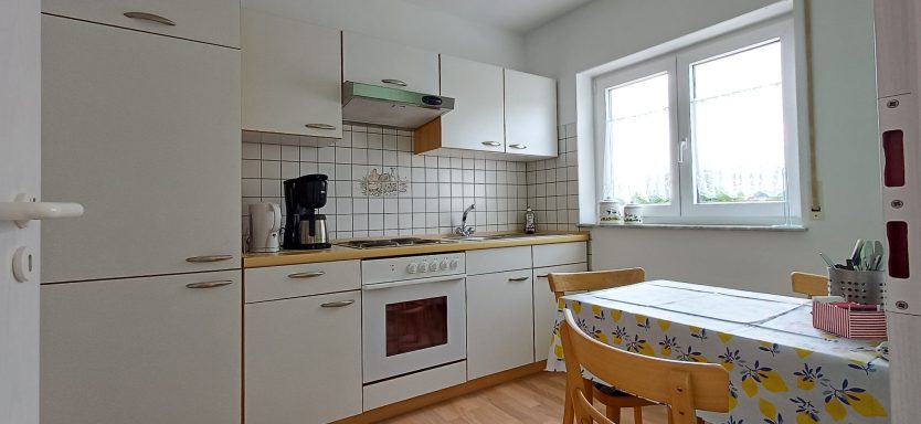 Küche Helle Küche mit weißem Mobiliar, Tisch und Stühlen, Fenster mit Blick nach draußen.