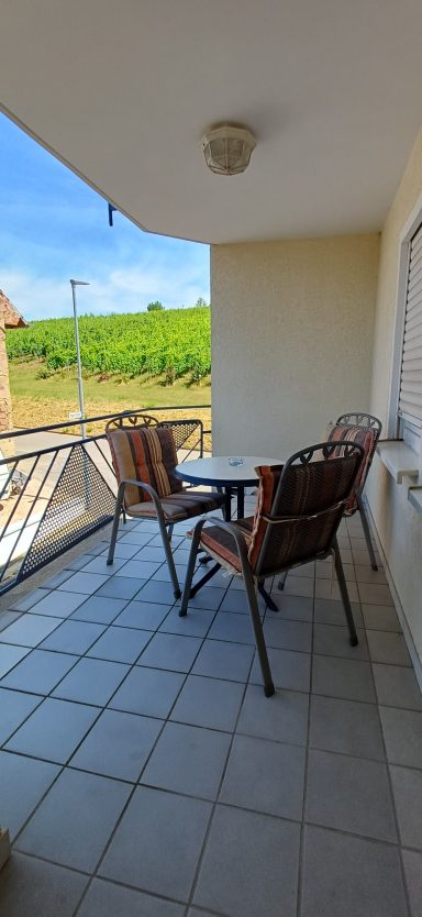 Balkon Balkon mit Tisch und Stühlen, Blick auf Weinberge und blauen Himmel.