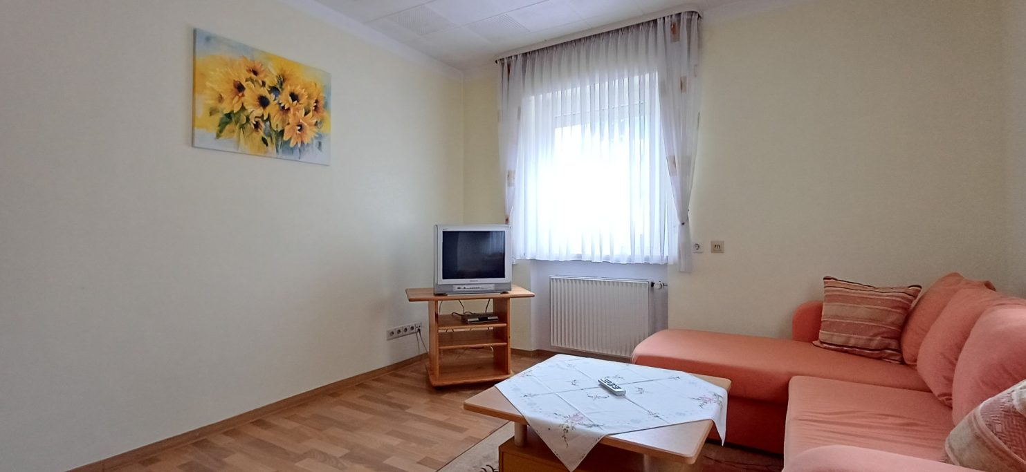 Wohnzimmer Heller Wohnraum mit Couch, Tisch und Fernseher, goldene Sonnenblumenmalerei an der Wand.